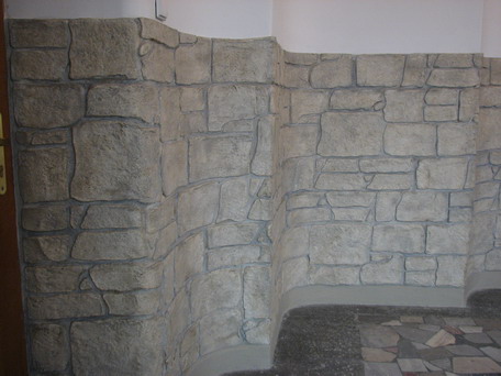 Ściana wewnętrzna wykończona betonem architektonicznym z odciskiem wzoru imitującego kamień, z widocznym zaokrąglonym narożnikiem i fragmentem podłogi z płytek.